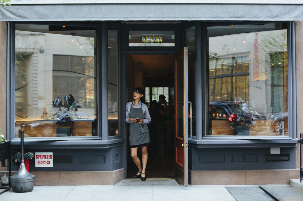 Young women wearing an apron stands in front of a cafe window